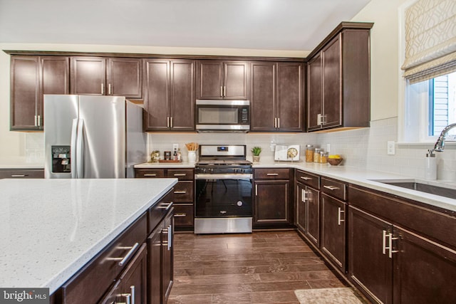 kitchen featuring stainless steel appliances, a sink, dark wood finished floors, and decorative backsplash