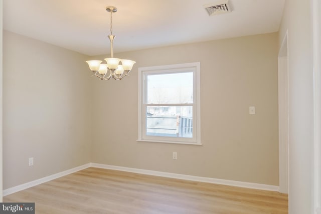 empty room with visible vents, a notable chandelier, light wood-style flooring, and baseboards