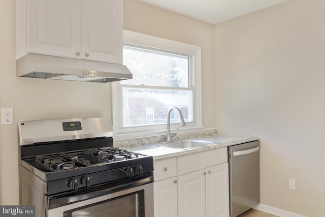 kitchen with stainless steel appliances, light countertops, white cabinets, a sink, and under cabinet range hood