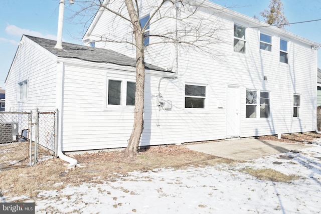 snow covered back of property featuring central AC and fence