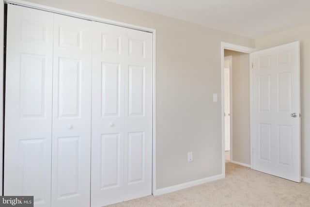 unfurnished bedroom with light carpet, a closet, and baseboards