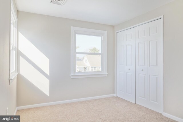 unfurnished bedroom with light carpet, a closet, visible vents, and baseboards