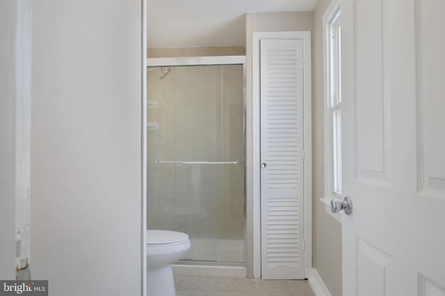 bathroom featuring baseboards, toilet, tile patterned flooring, a shower stall, and a closet