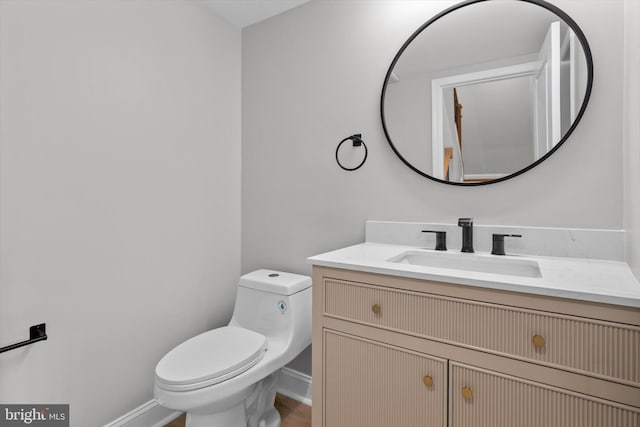 half bathroom with baseboards, vanity, and toilet