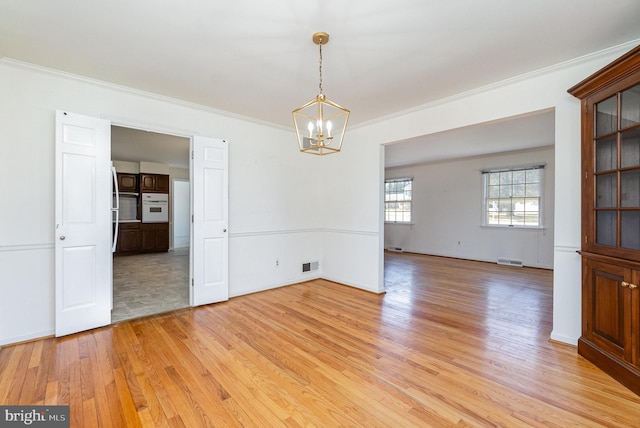 spare room with visible vents, an inviting chandelier, light wood-style flooring, and ornamental molding