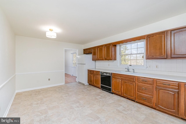 kitchen with a sink, black dishwasher, freestanding refrigerator, brown cabinetry, and light countertops