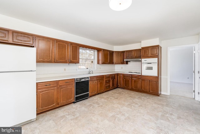 kitchen with tasteful backsplash, under cabinet range hood, light countertops, white appliances, and a sink