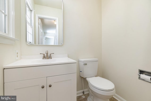 half bath with baseboards, toilet, and vanity