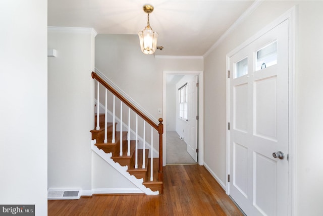 entryway with wood finished floors, visible vents, an inviting chandelier, stairs, and crown molding