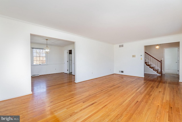 unfurnished living room with a notable chandelier, light wood-type flooring, stairs, and visible vents