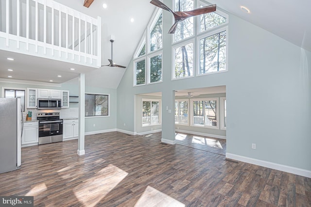 unfurnished living room with dark wood-type flooring, ceiling fan, high vaulted ceiling, and baseboards