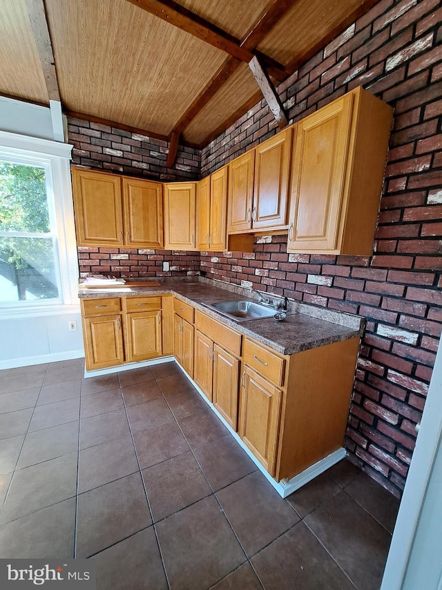 kitchen featuring wooden ceiling, brick wall, dark tile patterned floors, a sink, and dark countertops