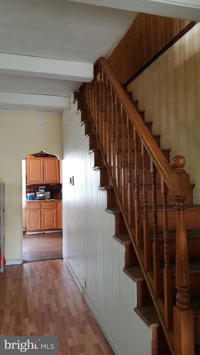 stairway with lofted ceiling with beams, wooden walls, and wood finished floors