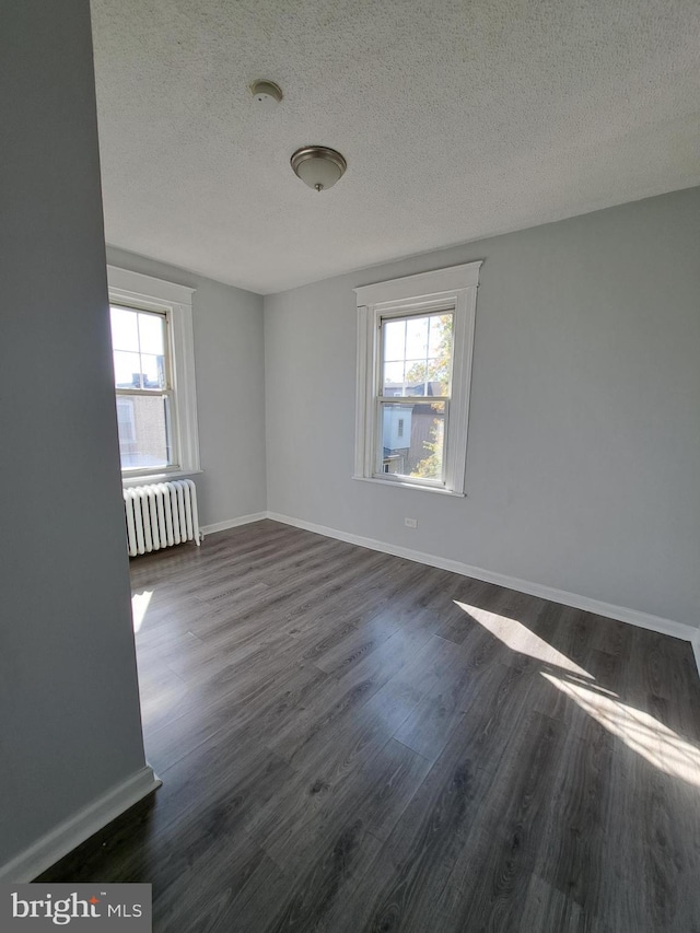 spare room with dark wood-style floors, a healthy amount of sunlight, baseboards, and radiator