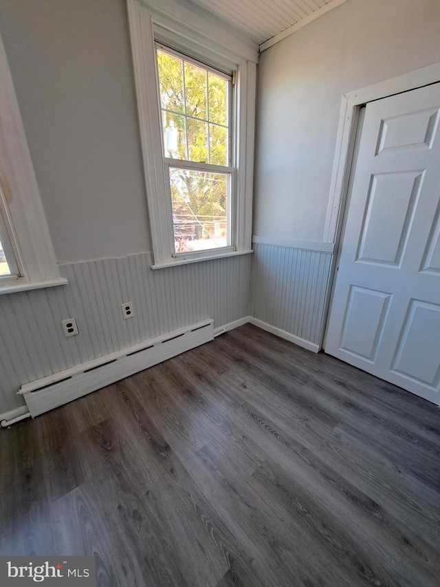 unfurnished room featuring a baseboard heating unit, a wainscoted wall, and dark wood-style floors