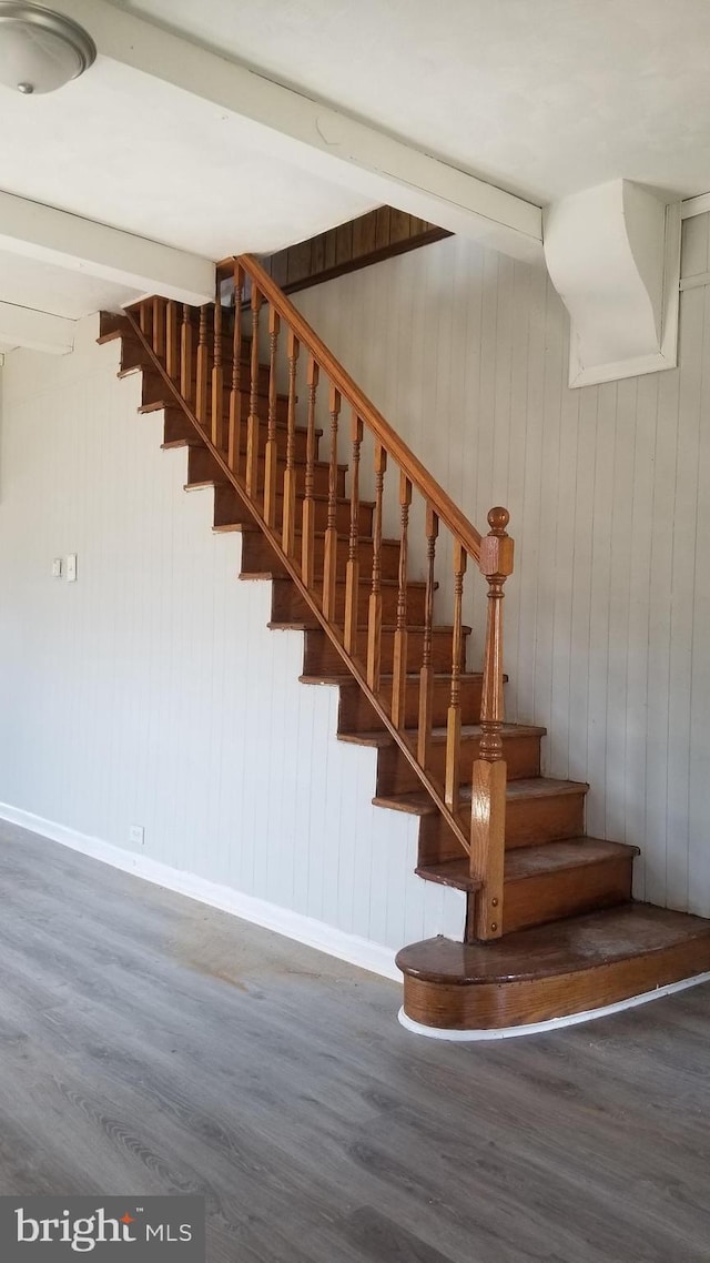 staircase featuring wood finished floors, beam ceiling, and baseboards