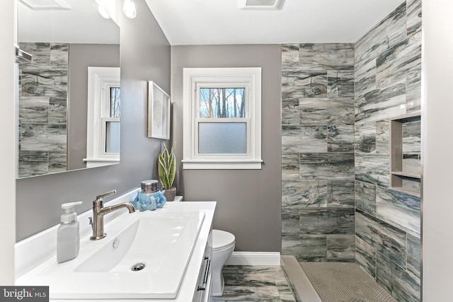 bathroom with toilet, a tile shower, vanity, and baseboards