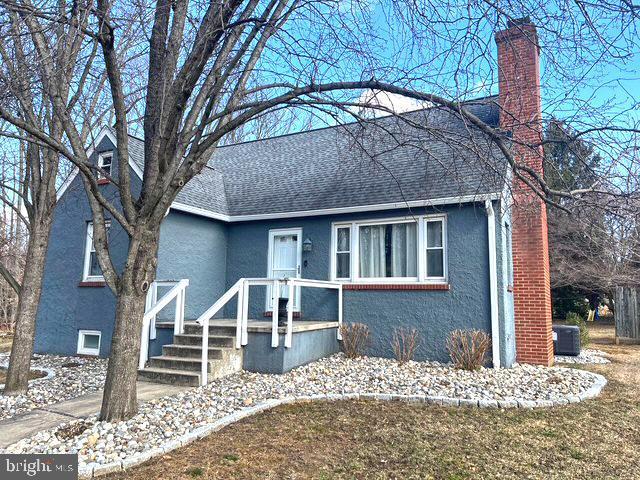 view of front of home with central AC, roof with shingles, a chimney, and stucco siding