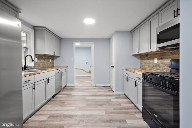 kitchen featuring light wood-style flooring, stainless steel appliances, gray cabinetry, wooden counters, and a sink