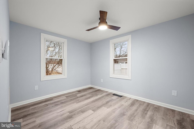 empty room with ceiling fan, wood finished floors, a wealth of natural light, and baseboards