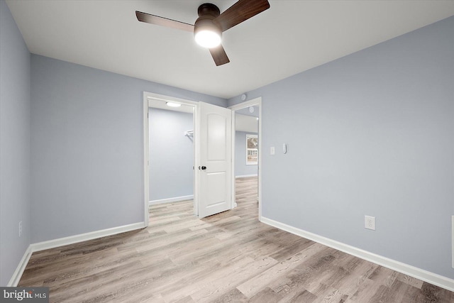 unfurnished bedroom with light wood finished floors, a closet, a walk in closet, and baseboards