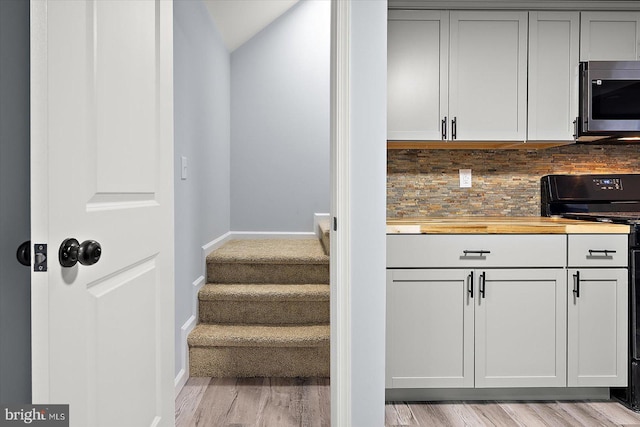 kitchen featuring butcher block counters, stainless steel microwave, electric range, light wood-style floors, and baseboards