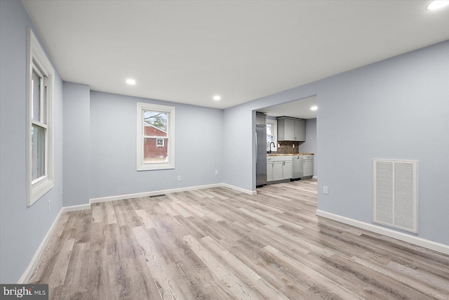 unfurnished living room with baseboards, visible vents, light wood-style floors, a sink, and recessed lighting