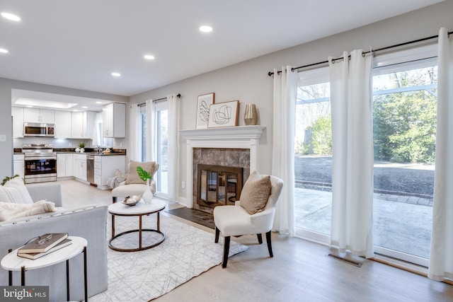 living area featuring light wood-style flooring, a tiled fireplace, visible vents, and recessed lighting