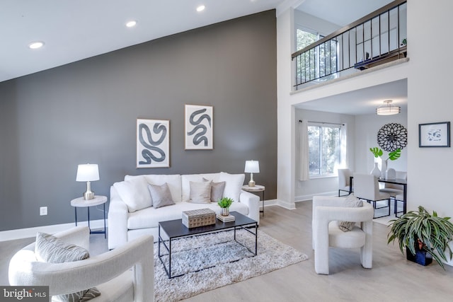 living area with a high ceiling, recessed lighting, wood finished floors, and baseboards