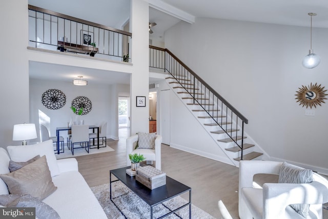 living area with baseboards, stairway, wood finished floors, beamed ceiling, and high vaulted ceiling