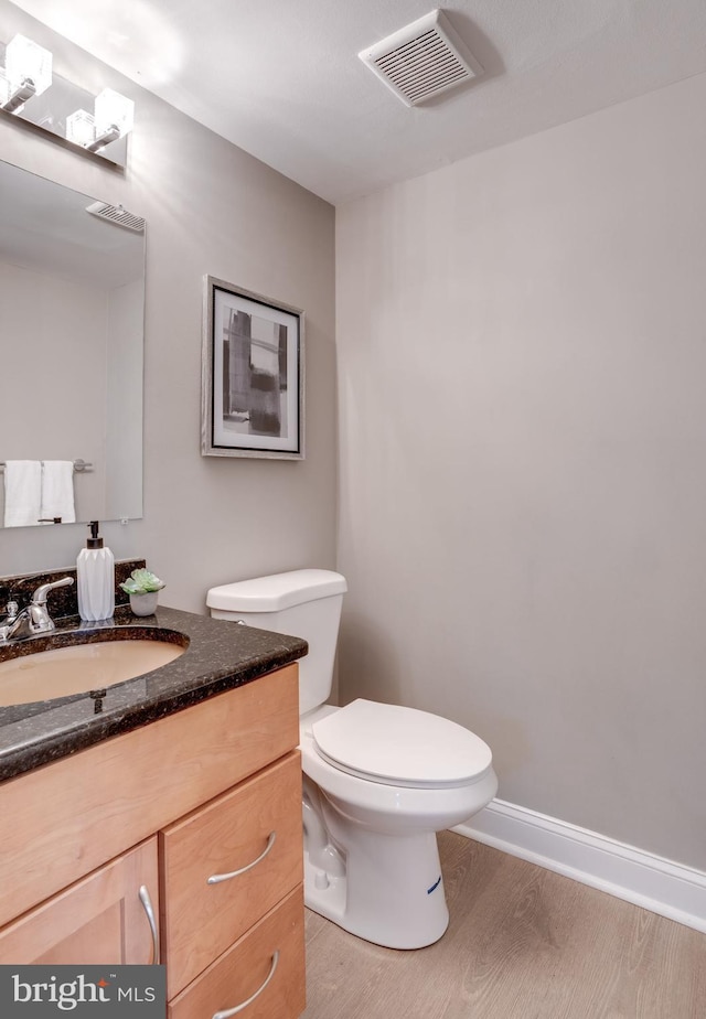 bathroom with visible vents, toilet, vanity, wood finished floors, and baseboards