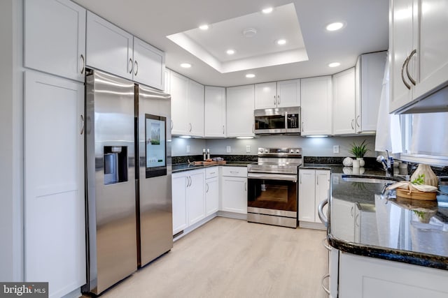 kitchen featuring light wood finished floors, a raised ceiling, appliances with stainless steel finishes, white cabinets, and a sink