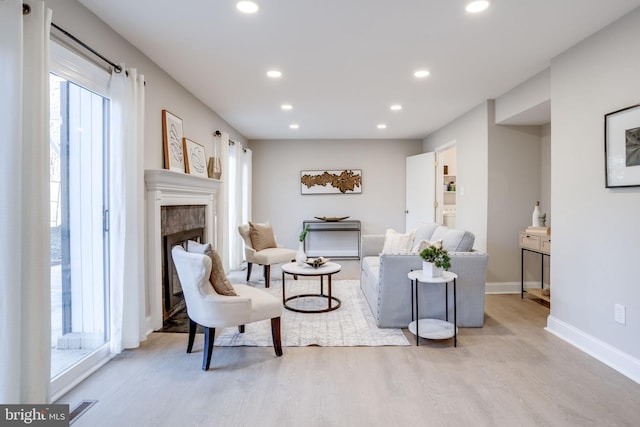 living room with a fireplace, light wood finished floors, recessed lighting, visible vents, and baseboards