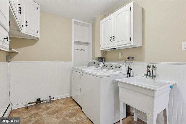 clothes washing area featuring cabinet space, baseboard heating, wainscoting, a sink, and separate washer and dryer