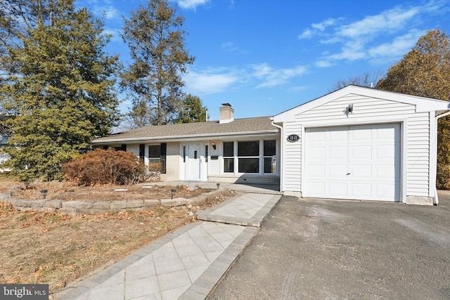 ranch-style home featuring a garage, driveway, a chimney, and a shingled roof