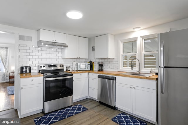 kitchen with under cabinet range hood, a sink, visible vents, wooden counters, and appliances with stainless steel finishes