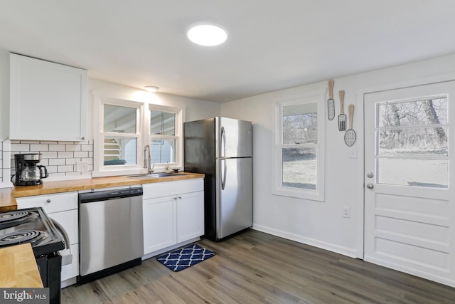 kitchen with butcher block countertops, appliances with stainless steel finishes, white cabinets, and a sink