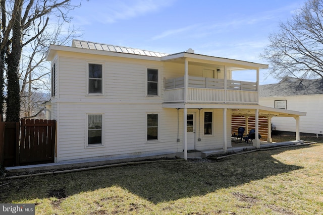 rear view of property featuring metal roof, a balcony, fence, a lawn, and a patio area