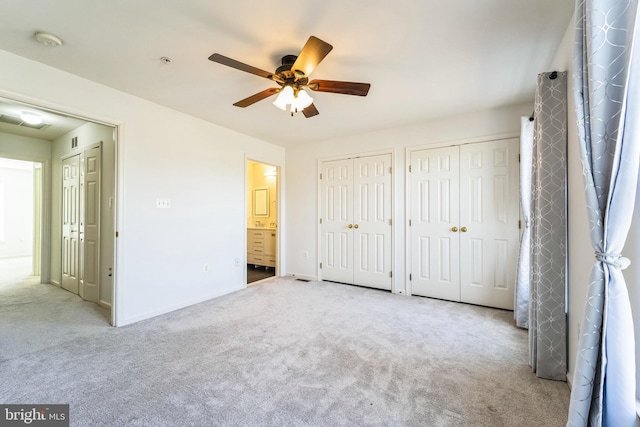 unfurnished bedroom featuring connected bathroom, carpet flooring, a ceiling fan, baseboards, and multiple closets