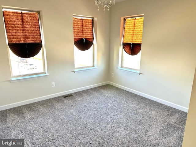 carpeted spare room featuring a chandelier, visible vents, and baseboards