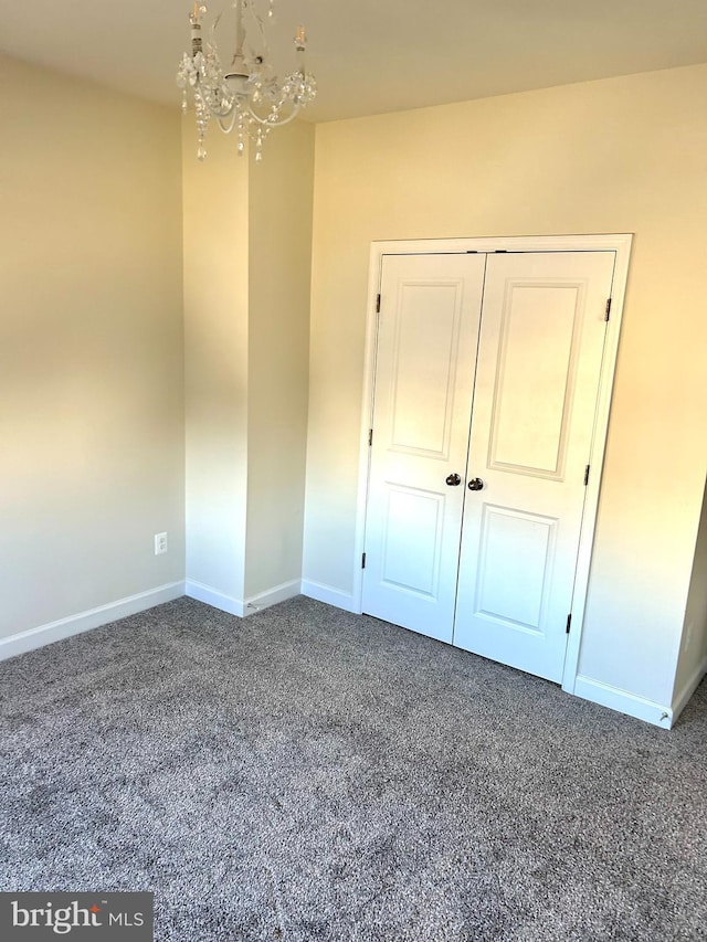 unfurnished bedroom with a closet, a notable chandelier, dark carpet, and baseboards