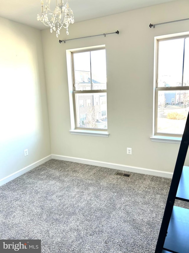 carpeted spare room featuring baseboards, a notable chandelier, visible vents, and a wealth of natural light