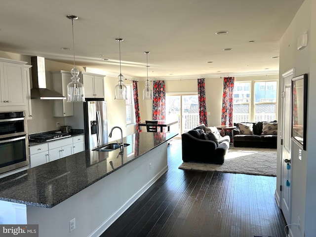 kitchen featuring white cabinets, wall chimney exhaust hood, appliances with stainless steel finishes, decorative light fixtures, and a sink