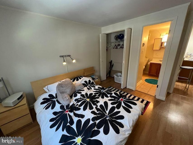 bedroom with ensuite bathroom, a closet, wood finished floors, and crown molding