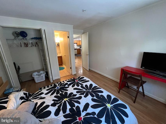 bedroom with connected bathroom, wood finished floors, baseboards, ornamental molding, and a closet