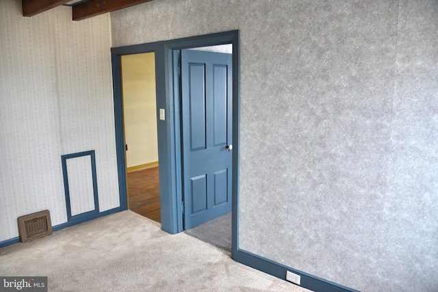 empty room featuring visible vents, baseboards, beam ceiling, carpet, and wallpapered walls