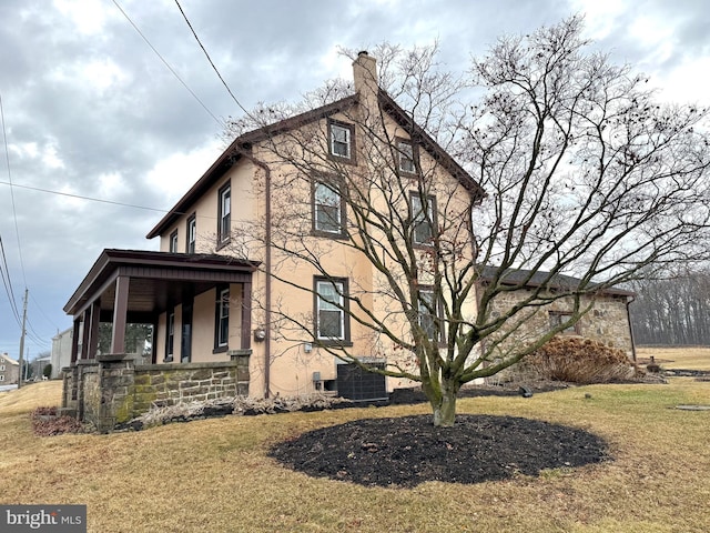 view of side of property featuring a chimney, a lawn, central AC unit, and stucco siding