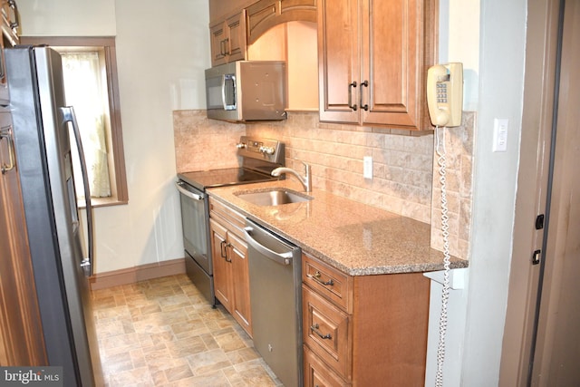 kitchen featuring stainless steel appliances, a sink, baseboards, stone finish flooring, and tasteful backsplash