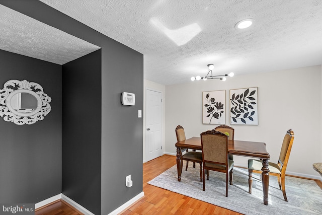 dining area with light wood finished floors, an inviting chandelier, a textured ceiling, and baseboards