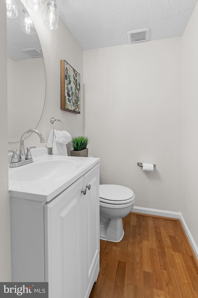 bathroom featuring visible vents, toilet, vanity, wood finished floors, and a textured ceiling